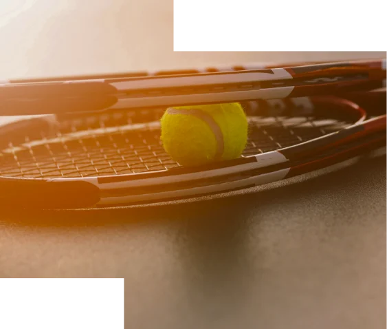 Deux raquettes de tennis et une balle jaune reposent sur un court baigné de soleil. La lumière chaude et le flou artistique évoquent un sentiment de calme et d'anticipation